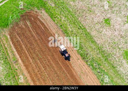 Il trattore aratri un piccolo campo nel villaggio prima di piantare verdure. Vista dell'altezza dell'antenna Foto Stock