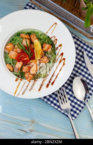 Tagliatelle di riso con salmone e spinaci. Pranzo in un piatto bianco sul tavolo. Pomodori, limone, pesce, rosmarino, semi di soi e sesamo. Cibo ancora vita Foto Stock