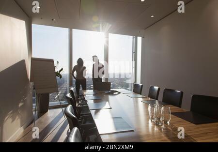 Gli uomini d'affari parlano alla luminosa e alta finestra della sala conferenze Foto Stock