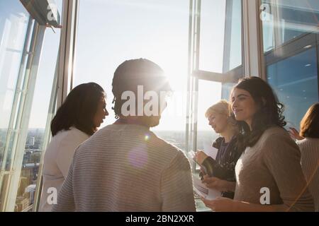 Persone in viaggio d'affari che parlano alla soleggiata finestra dell'ufficio Foto Stock