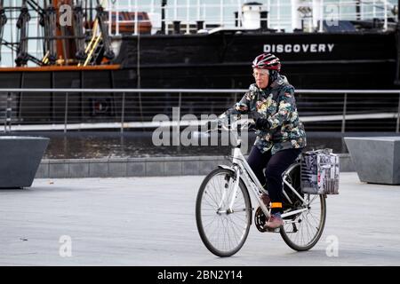 Dundee, Tayside, Scozia, Regno Unito. 12 maggio 2020. Tempo nel Regno Unito: Una giornata di sole e nuvoloso con incantesimi a Dundee Scozia con temperatura massima 12°C.. Una donna anziana che gode del clima fresco mentre prende le esercitazioni esterne leggere che cavalcano la sua bicicletta di Ridgeback oltre la nave di scoperta di RRS lungo il lungomare durante le limitazioni di bloccaggio di Covid-19. Credit: Dundee Photographics/Alamy Live News Foto Stock