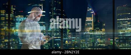 Scienziato maschile in tuta pulita che lavora tardi nella finestra della città Foto Stock