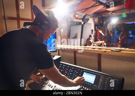 Uomo che lavora alla sound board in studio di registrazione musicale Foto Stock