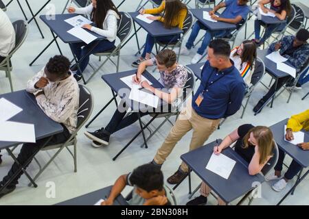 Insegnante che supervisiona gli studenti delle scuole superiori che si stanno studiando presso le scrivanie Foto Stock