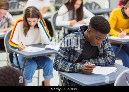 Studente di scuola superiore che si occupa di esami alla scrivania in classe Foto Stock