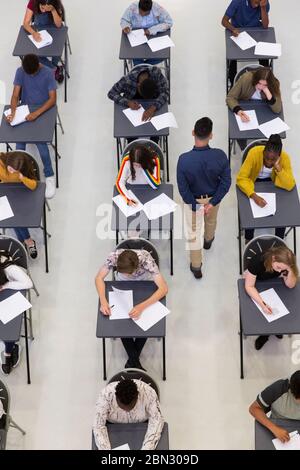 Insegnante che supervisiona gli studenti delle scuole superiori che si stanno studiando presso le scrivanie Foto Stock