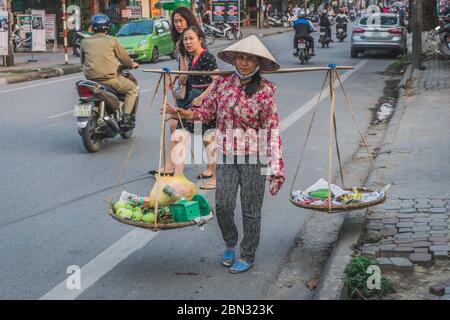 Una donna in abiti tradizionali vietnamiti vende frutta e verdura in città Foto Stock