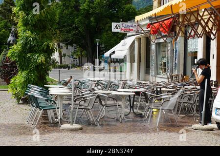 I ristoranti italiani di Merano, in Alto Adige, sono ancora chiusi a causa del COVID-19. Sedie e tavoli impilati e incatenati insieme. Pulizia da donna Foto Stock