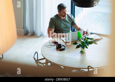 Uomo che usa un computer portatile, che lavora da casa al tavolo da pranzo Foto Stock