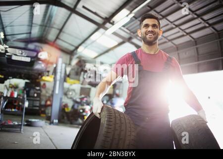 Ritratto sorridente meccanico maschile che trasporta pneumatici in officina di riparazione auto Foto Stock