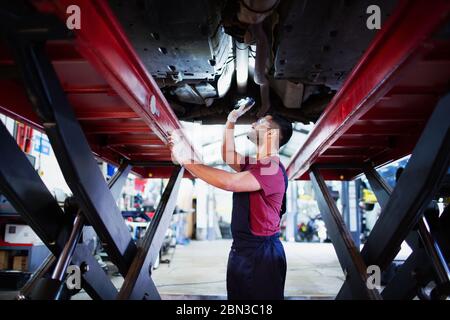 Meccanico maschile con torcia sotto l'auto in officina di riparazione auto Foto Stock