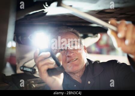 Meccanico maschile con torcia che lavora sotto l'auto in officina di riparazione auto Foto Stock