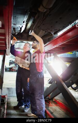 Meccanici maschi che lavorano sotto l'auto in officina di riparazione auto Foto Stock