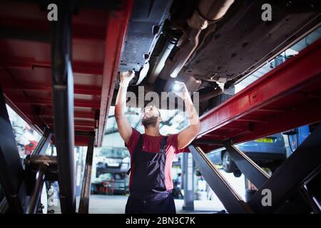 Meccanico maschile con torcia che lavora sotto l'auto in officina di riparazione auto Foto Stock