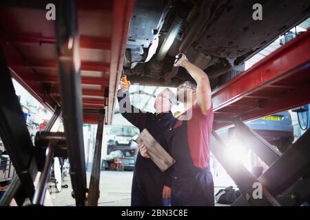 Meccanici maschili con torcia che lavora sotto l'automobile in officina di riparazione auto Foto Stock