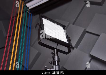 l'assistente di studio fissa la luce video professionale sul supporto luminoso regolabile. Lampada LED su treppiede in studio fotografico. Lampada per foto e video su wal grigio goffrato Foto Stock