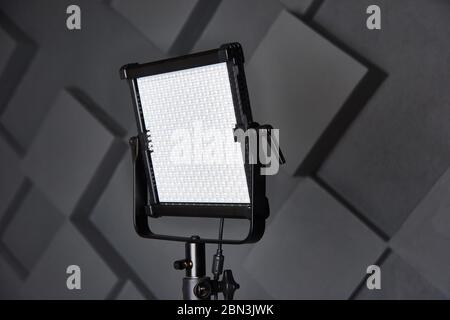 l'assistente di studio fissa la luce video professionale sul supporto luminoso regolabile. Lampada LED su treppiede in studio fotografico. Lampada per foto e video su wal grigio goffrato Foto Stock