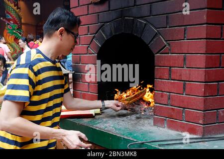 Tempio taoista di Guan di chinese. Uomo che brucia carta di joss offerte in forno. Kuala Lumpur. Malesia. Foto Stock