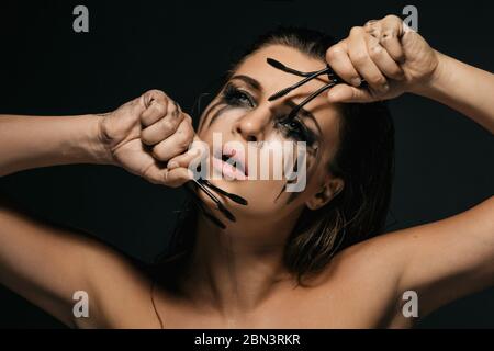 Bella donna con sbavature di trucco sul suo viso e spazzole mascara rotte Foto Stock