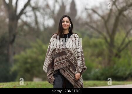 Giovane donna con carnagione abbronzata che indossa poncho nel parco e sorridente. Foto Stock