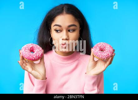 Donna affamata pensierosa che sceglie tra le ciambelle. Cibo di tentazione. Concetto di dieta Foto Stock