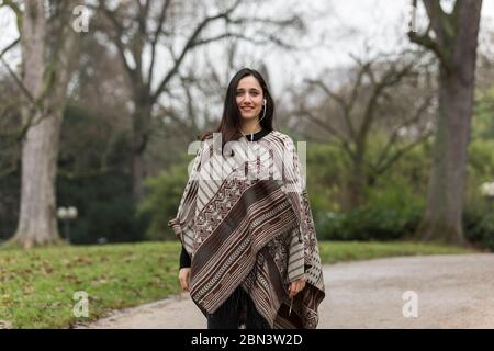 Bella donna indiana che indossa poncho sorridente alla macchina fotografica. Sfondo del parco autunnale. Foto Stock