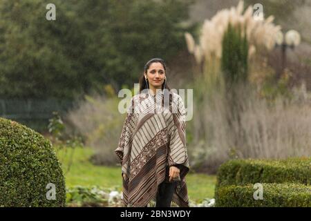 Bella donna indiana che indossa poncho in posa in giardino ornamentale. Guardando lontano. Foto Stock