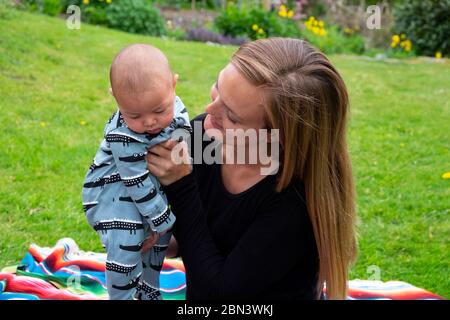 Vita in blocco covid 19 2020 per la madre seduta in giardino di campagna sorridente a 3 mesi bambino ragazzo fuori a maggio Sunshine Galles UK KATHY DEWITT Foto Stock