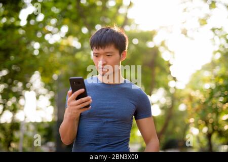 Ritratto di giovane asiatico utilizzando il telefono al parco all'aperto Foto Stock