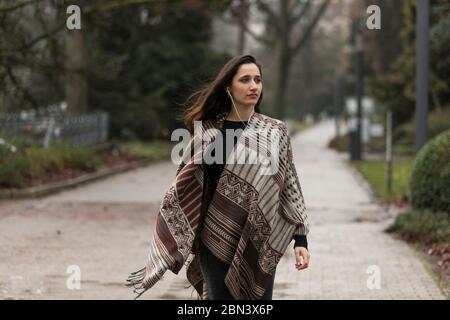 Giovane donna indiana che indossa poncho camminare all'aperto con la testa girata guardando via. Foto Stock