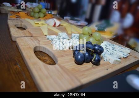 Primo piano di formaggio brie a muffa blu con uve su un piatto di legno con vari altri formaggi e frutta sullo sfondo preparato per un formaggio t Foto Stock