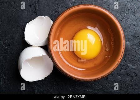 Tuorlo di pollo da uova organiche rotte in piastra marrone su fondo di cemento nero. Fotografia alimentare Foto Stock
