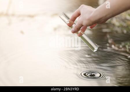 Concetto di inquinamento dell'acqua dello stagno. Il biologo e ricercatore scienziato preleva campioni di acqua sporca da uno stagno in una provetta Foto Stock