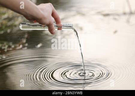 Concetto di inquinamento dell'acqua dello stagno. Il biologo e ricercatore scienziato preleva campioni di acqua sporca da uno stagno in una provetta Foto Stock