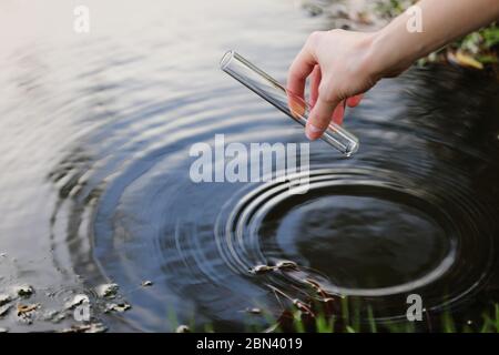 L'idrobiologo scienziato e biologo preleva campioni d'acqua per l'analisi. La mano raccoglie l'acqua in una provetta. Concetto di inquinamento dell'acqua dello stagno Foto Stock