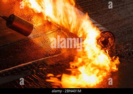 Posa in opera di rivestimenti bitumati dal rotolo con una fiamma di bruciatore di close-up. Foto Stock