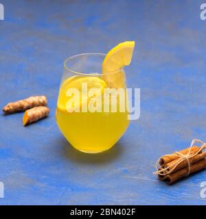 Tè freddo allo zenzero curcuma fatto in casa con cannella e limone in una tazza di vetro su sfondo blu Foto Stock