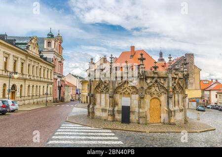 Fontana di pietra nel centro storico di Kutna Hora con strada acciottolata, edifici di vecchio stile, sfondo blu cielo nuvoloso, Boemia Centrale, Repubblica Ceca Foto Stock