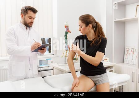 Medico maschile che esamina la paziente femminile che soffre di dolore al gomito. Esame medico. Chiropratica, osteopatia, riabilitazione post traumatica, sport fisico Foto Stock