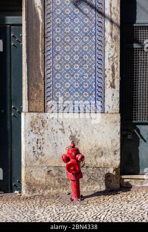 Un idrante rosso si trova di fronte a un muro parzialmente piastrellato su una strada a Lisbona, in Portogallo Foto Stock