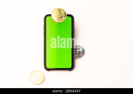 Criptovaluta monete bitcoin colorate fisiche. Moneta dorata con telefono cellulare con schermo verde su sfondo bianco. Foto Stock