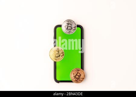 Faccia e retro della moneta criptovaluta dorata bitcoin e telefono con schermo verde isolato su sfondo bianco Foto Stock