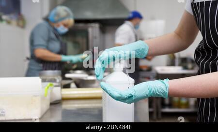 Portare via i lavoratori della cucina disinfettando le mani con un detergente spray Foto Stock