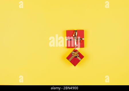 Due scatole regalo rosse con nastro dorato su sfondo giallo. Vista superiore, spazio per la copia, mock up, disposizione piatta. Natale, anno nuovo, compleanno, vacanza. Festa b Foto Stock