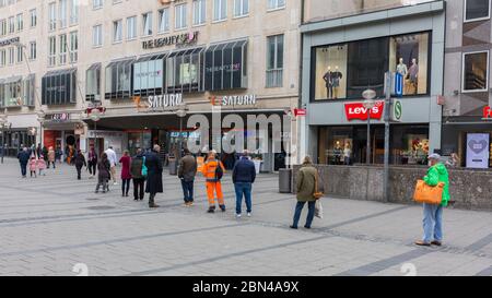 Persone che si accodano all'ingresso del mercato di Saturno (rivenditore di elettronica) a Karlsplatz / Stachus (centro di Monaco). Foto Stock