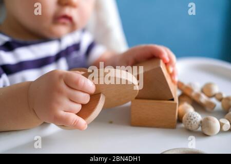 giocattoli eco legno. gioco per bambini. Bambino caucasico poco intelligente che gioca giochi naturali su seggiolone. Giochi per lo sviluppo precoce. Giocattolo nelle mani dei bambini da vicino. Foto Stock