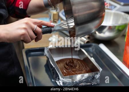 Donna che versa l'impasto di cioccolato in una padella Foto Stock