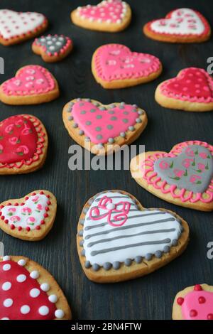 Immagine verticale di biscotti a base di ghiaccio reali a forma di cuore sparsi su sfondo di legno marrone scuro Foto Stock