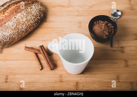 Piatto adagiato su tavola di legno di tazza nera con cacao, pane e cannella Foto Stock