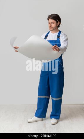 Ritratto a tutta lunghezza di giovane ingegnere edile che controlla progetto o piano di costruzione Foto Stock
